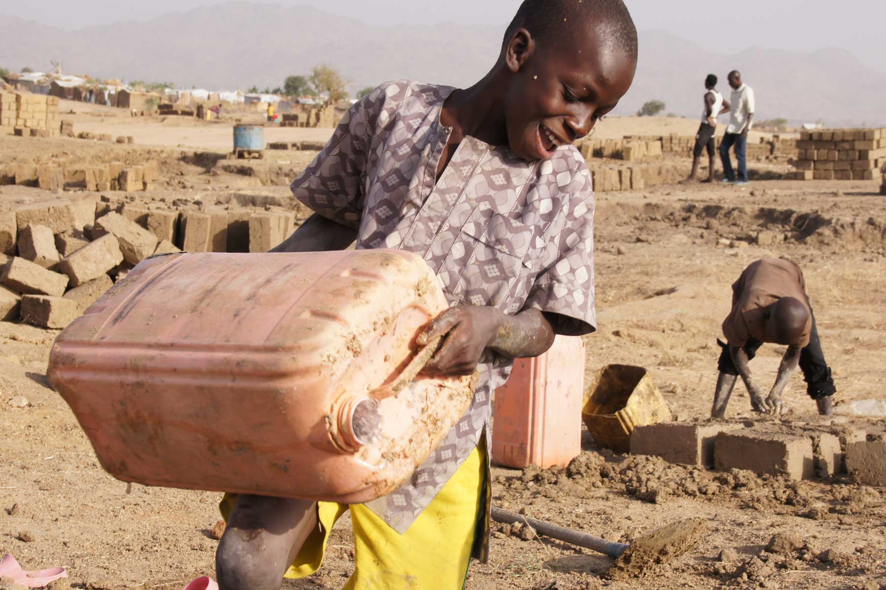 At the tap stand, predominantly women and girls wait to fill their jerry cans to cook and wash for the families.