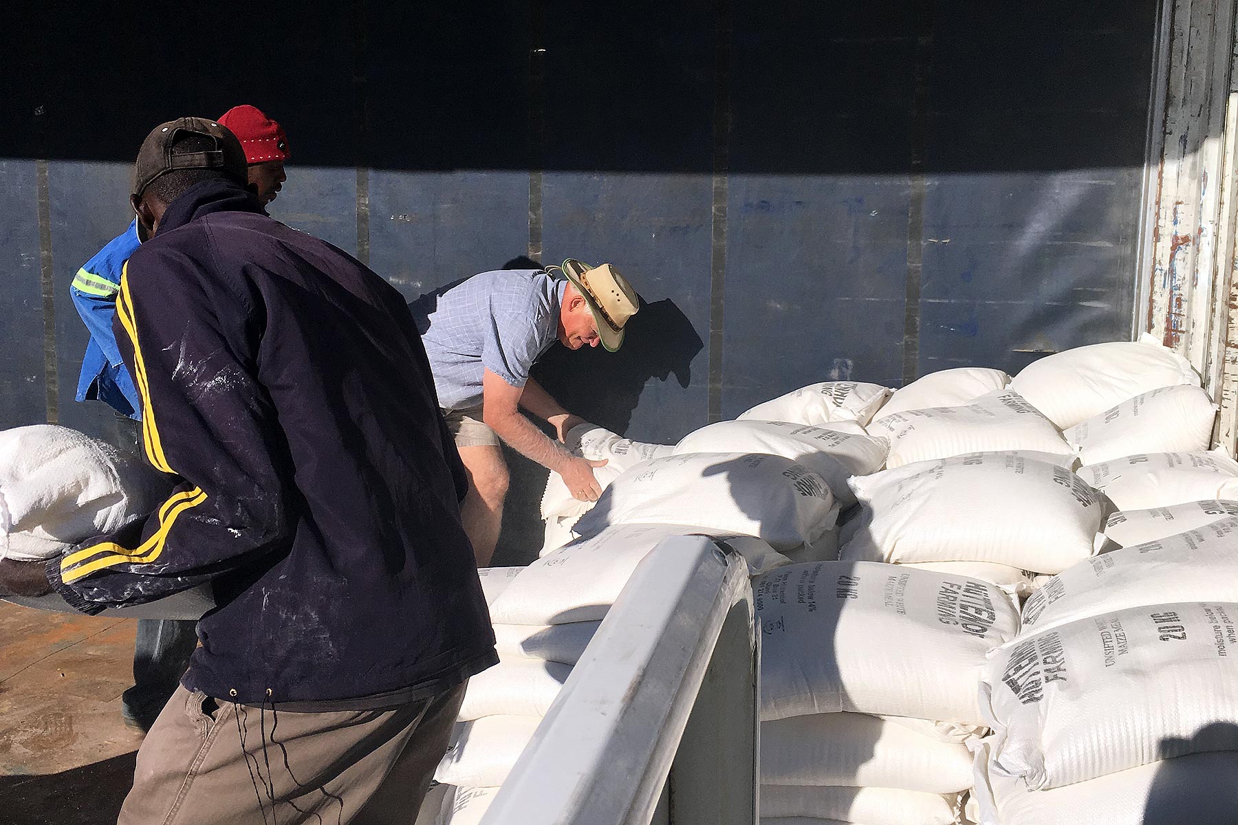 Many helping hands unloading maize meal and beans from the trucks.