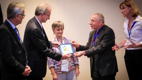 Marcia Blasi, Evangelical Church of the Lutheran Confession in Brazil, LWF General Secretary Martin Junge and Regional Program Coordinator Anne Caroline Tevoy look on as Bishop Munib Younan presents a decorative tile of the LWF Assembly logo to the Rev. Dr. Nestor Paulo Friedrich, Evangelical Church of the Lutheran Confession in Brazil. The Brazilian church made a gift to the AVH Hospital and the tile is a token of thanks. Photo: LWF/Johanan Celine Valeriano