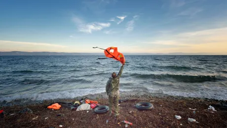 A Greek volunteer waves at a refugee boat in the Aegean Sea, directing it toward a safe place to land on a beach on the Greek island of Lesbos. Photo: Paul Jeffrey