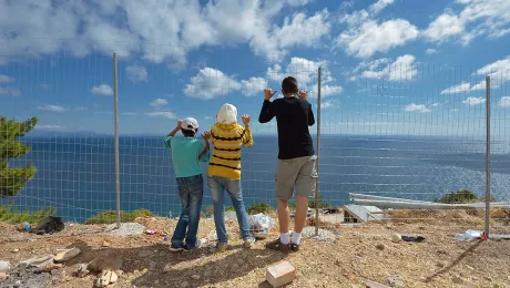 Syrian refugee children at a fence facing the Aegean Sea coast, Greece. Photo: ACT/ Paul Jeffrey