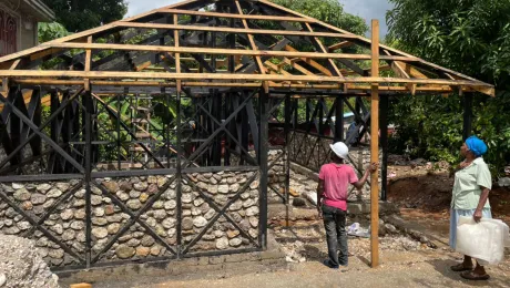 As part of the housing construction project, participants provide rocks, wood and food for the construction workers. Marie Nusia, a project participant, observes the progress on her new hurricane and earthquake resistant home. Photo: LWF Haiti