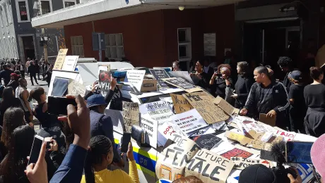 The anti-femicide demonstration in Cape Town, South Africa following the death of Uyinene Mrwetyana. Protestors cover a police vehicle with placards. Photo: Discott, via Wikimedia Commons (CC-BY-SA)