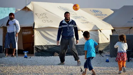 A man plays football with his children in the Zaatari Refugee Camp, Jordan, while another man, wounded in fighting in Syria, looks on. Photo: Paul Jeffrey/ACT