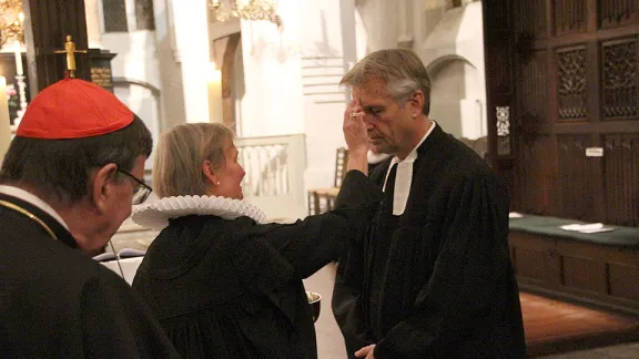 Bischöfin Kirsten Fehrs (Mi.) von der Evangelisch-Lutherischen Kirche in Norddeutschland zeichnet während des Gottesdienstes im Rahmen der Tagung der VELKD-Generalsynode 2012 als symbolische Tauferinnerung ein Kreuz auf die Stirn von LWB-Generalsekretär Pfr. Martin Junge. Links im Bild Kurt Kardinal Koch, Präsident des Päpstlichen Rates zur Förderung der Einheit der Christen. © LWB/DNK