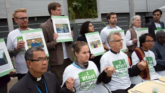 An interfaith group of religious leaders sits in front of empty trays during a public action at COP21 in Paris in 2015. Photo: LWF/Ryan Rodrick Beiler