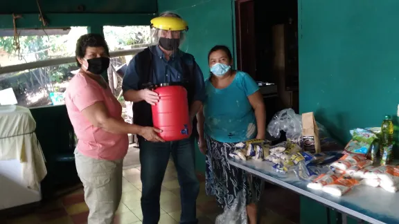 Hans-Jürgen Johnke (mitte), Mission EineWelt-Mitarbeiter in El Salvador übergibt Lebensmittel und einen Kanister zur Handreinigung an Gemeindemitglieder in El Volcan. Foto: MEW