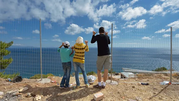 Syrische Flüchtlingskinder blicken durch einen Zaun über die Ägäis, Griechenland. Foto: ACT/ Paul Jeffrey