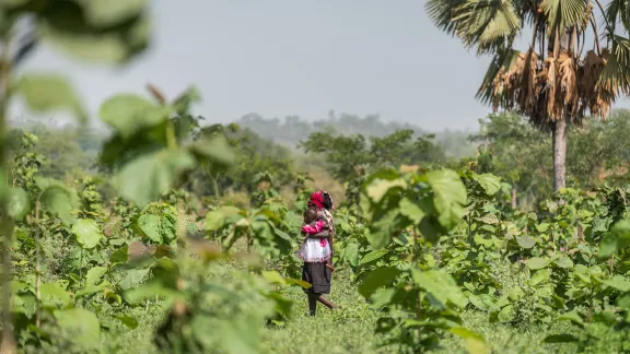 Uganda: A woman walks with her child through a tree plantation field in the Palorinya refugee settlement in the West Nile area of northern Uganda. The settlement hosts more than 128,000 refugees who arrived following the eruption of war in South Sudan in 2013. The refugees and host communities in the area receive support from the LWF World Service program in Uganda. Photo: LWF/Albin HillertÂ 