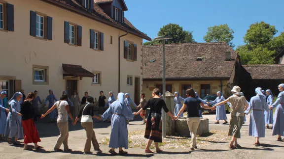 Schwestern der Kommunität Grandchamp und Gäste der monastischen Gemeinschaft halten sich vor Beginn der Corona-Pandemie an den Händen. Foto: Grandchamp Community