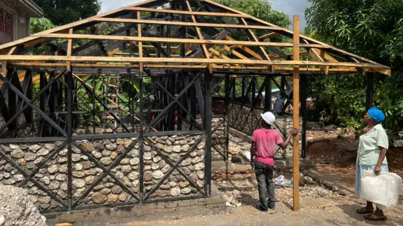 Im Rahmen des Wohnungsbauprojekts stellen die Teilnehmenden Steine, Holz und Lebensmittel für die Bauarbeiter zur Verfügung. Marie Nusia, eine Projektteilnehmerin, beobachtet den Fortschritt beim Bau ihres neuen hurrikan- und erdbebensicheren Hauses. Foto: LWB Haiti