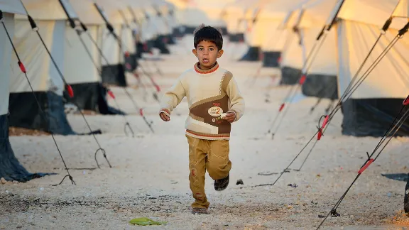 Early in the morning, a boy runs amid the tents in the Zaatari Refugee Camp, located near Mafraq, Jordan. Opened in July, 2012, the camp holds upwards of 20,000 refugees from the civil war inside Syria, but its numbers are growing. Photo: Paul Jeffrey/ACT