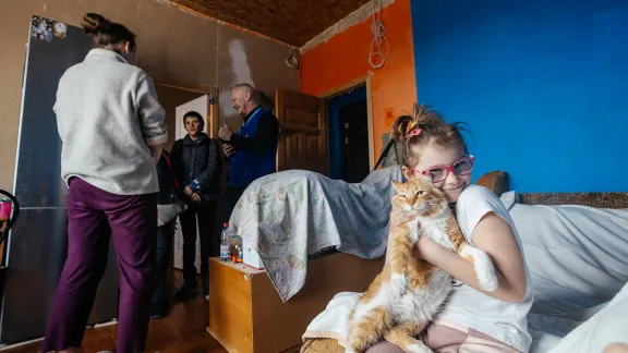 A girl holds her cat while an LWF team discusses reconstruction needs with her mother. Photo: LWF/ Anantoliy Nazarenko