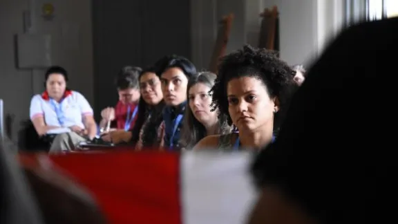 Los participantes escuchan atentamente a la representante de la iglesia del Perú, que con una bandera de su país en sus manos, relata la difícil situación que deben enfrentar los jóvenes que son reprimidos por las fuerzas policiales. Foto: LWF/Eugenio Albrecht